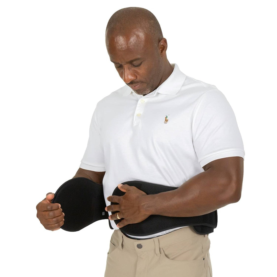 A man in a white polo shirt and beige pants is adjusting a Vive Health 627 LSO Pro Coretech lumbar brace around his waist. He appears focused on ensuring the compression pulley system fits comfortably for optimal trunk stability. The background is plain white.