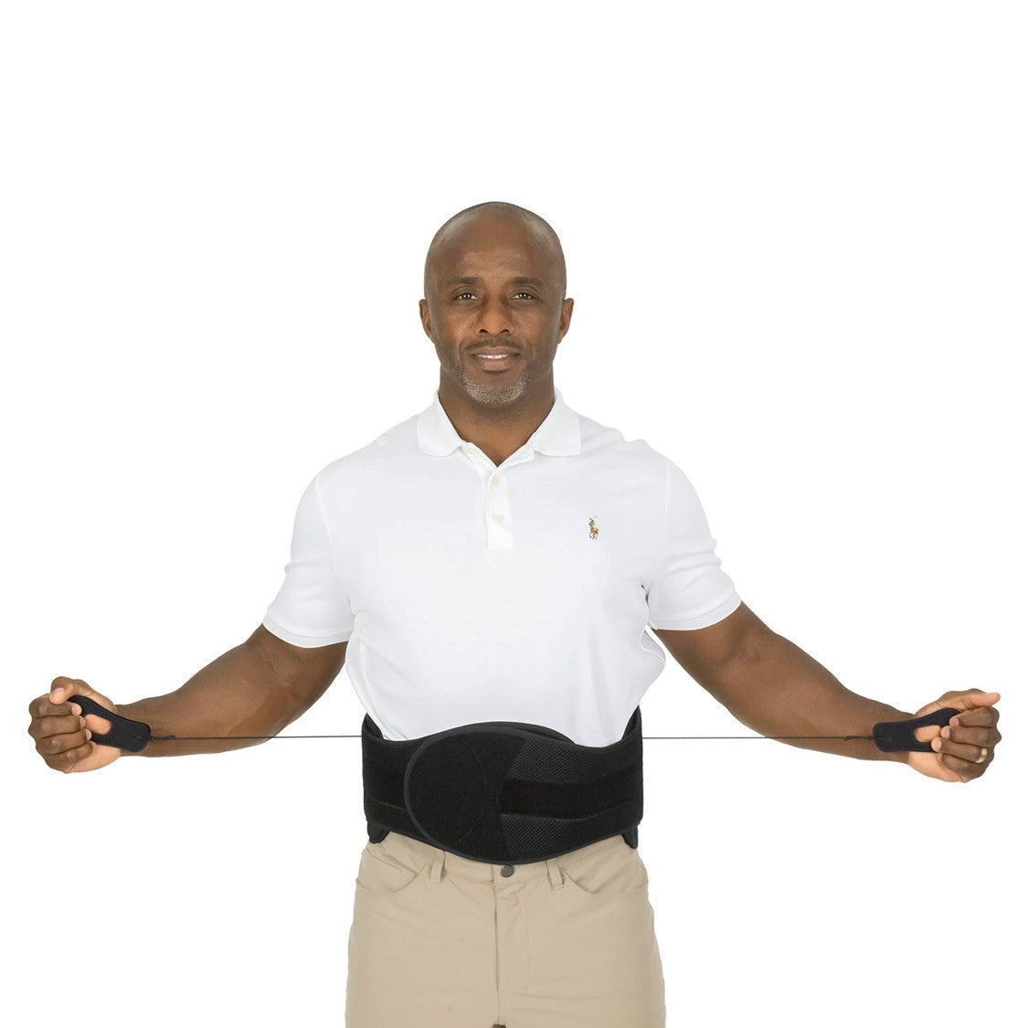 A man wearing a white polo shirt and beige pants demonstrates the use of the Vive Health 627 LSO Pro Coretech lumbar brace, adjusting the black straps to securely fit it around his lower back for enhanced trunk stability. The background is plain white.