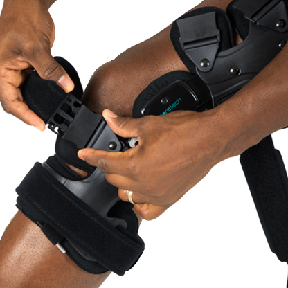 A person wearing the 845 Dual OA Knee Brace Coretech by Vive Health adjusts its straps to ensure a snug fit, aiming for improved mobility and pain relief.