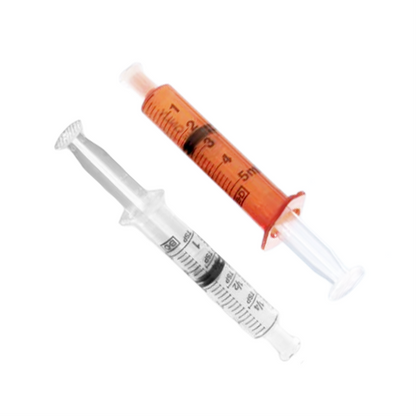 Two Becton Dickinson oral syringes on a white background: one is filled with red liquid and inverted, the other stands upright and empty. Both have clear plastic bodies with measurement markings.