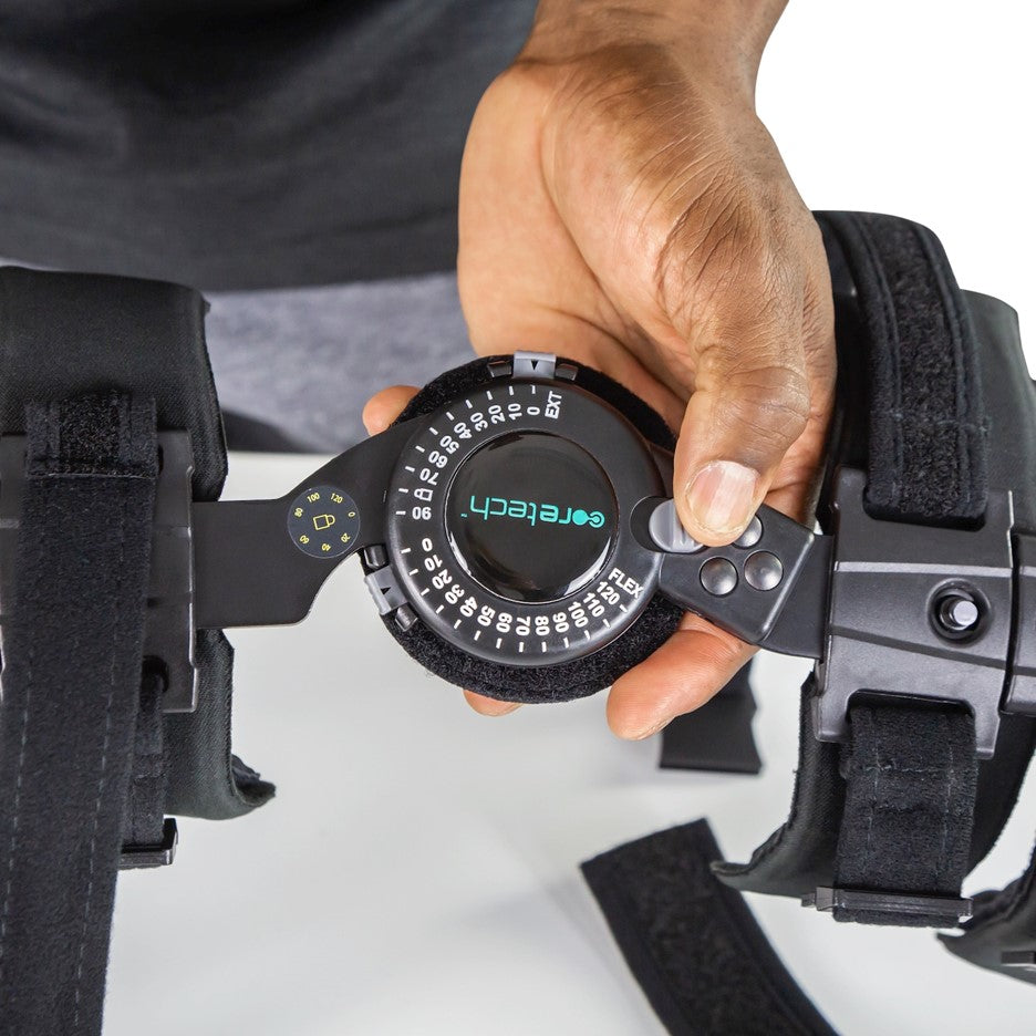 A person adjusts a hinge on an elbow brace, marked with the brand name "Vive Health," ensuring controlled range of motion. The black brace, named ROM Elbow Brace Coretech, features various straps and buckles as the person uses their fingers to turn a dial on it. The background is plain white.