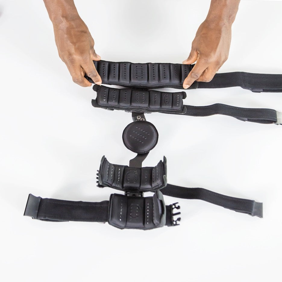 A person positions a Vive Health ROM Elbow Brace Coretech, in black with adjustable buckles and straps, on a white surface for optimal rehabilitative support.