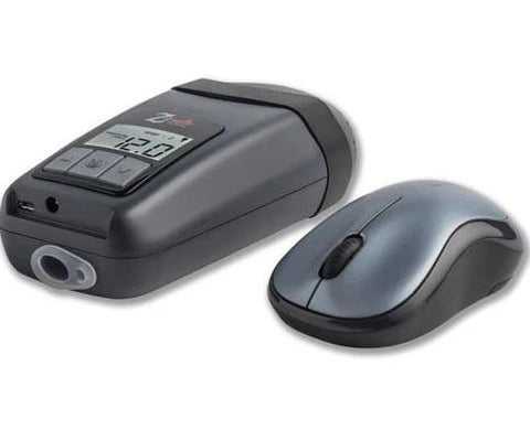 A gray electronic breathalyzer with a digital display sits beside a gray and black wireless computer mouse, resembling the sleek design of a Breas Z2 Auto CPAP Travel Device. The breathalyzer shows a reading on its screen and features a mouthpiece at one end.