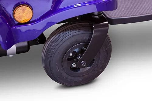 The EW-M51 Power Chair from E-Wheels features a close-up of its front wheel with a purple fender, highlighting its stable suspension. A black treaded wheel is attached to a rotating support fork, and an amber reflector is mounted above the wheel on the fender.