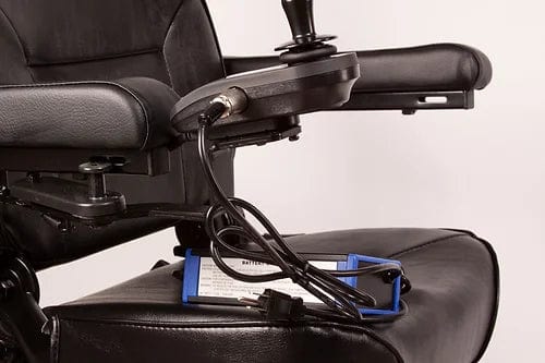 A close-up of the EW-M31 Compact Power Chair by E-Wheels, showcasing its sleek black electric design with joystick controls and connected wires on the armrest. This power chair features a black leather finish, complemented by a blue clipboard underneath it, emphasizing its versatile indoor/outdoor functionality.