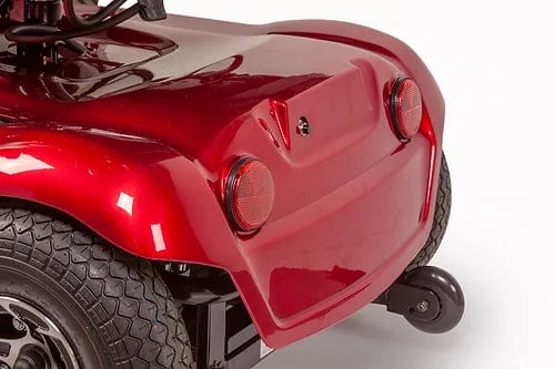 Close-up of the shiny red EW-M31 Compact Power Chair by E-Wheels, featuring two rear wheels and a small anti-tip wheel. Ideal for both indoor and outdoor use, it comes equipped with round rear lights, an adjustable headrest, and a sleek, curved design.