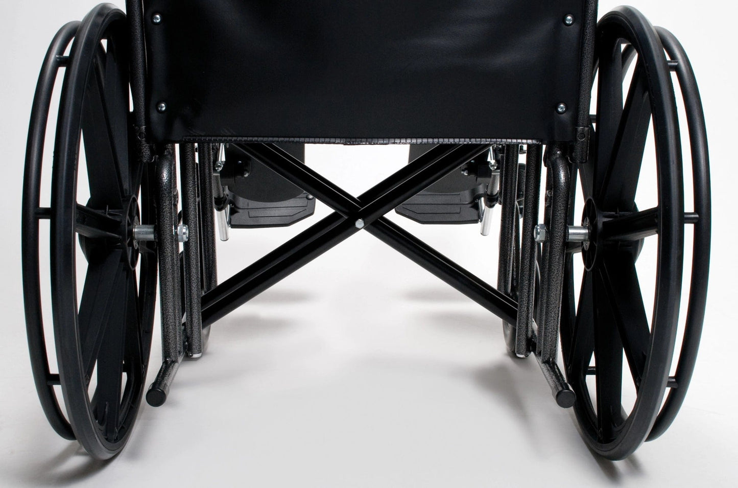 Close-up of the Traveler HD by Graham Field, a heavy-duty wheelchair viewed from the back. The image highlights its large wheels, footrests, and reinforced X-shaped frame beneath the seat. The background is a plain, white surface.