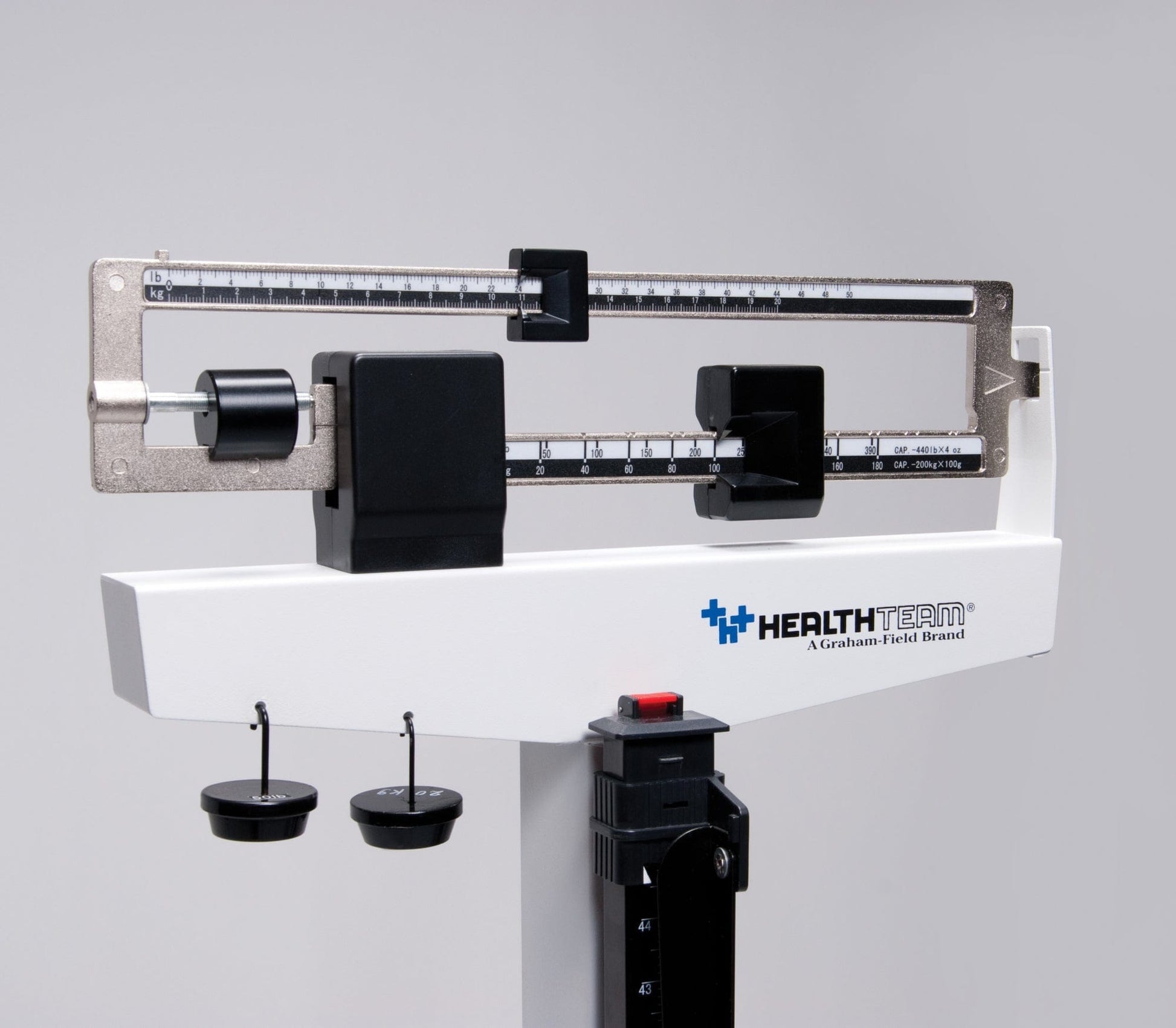 A close-up of a Graham Field Physician Mechanical Beam Scale with Wheels, featuring dual measurement indicators and sliding weights, shows off its impressive 490 lb weight capacity. The scale is set against a neutral gray background.