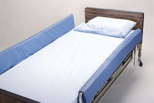 A hospital bed featuring blue side rails and a white sheet is placed in a room with a plain beige background. The headboard is wooden, with a pillow positioned at the head of the bed. For added safety, consider incorporating the Skil-Care Corporation's Bed Rail Pad 60" into this arrangement.